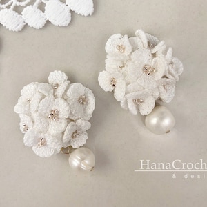 May include: A pair of white crocheted flower earrings with pearl accents. The earrings are delicate and feminine, and would be a beautiful addition to any outfit.