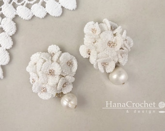 Puede incluir: Un par de pendientes de flores de ganchillo blanco con detalles de perlas. Los pendientes son delicados y femeninos, y serían una hermosa adición a cualquier atuendo.