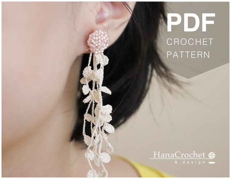 May include: A close-up of a person wearing a pair of long, white crochet earrings with a pink bead at the top. The earrings are hanging from the person's earlobe. The text "PDF CROCHET PATTERN" is visible in the upper right corner of the image. The text "HanaCrochet & design" is visible in the lower right corner of the image.