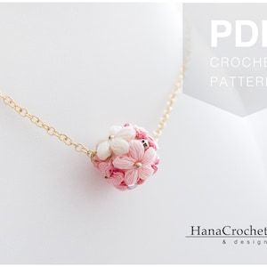 May include: A delicate gold chain necklace with a pink and white crocheted flower pendant. The pendant is made of small, tightly woven flowers and is a beautiful example of handmade jewelry.