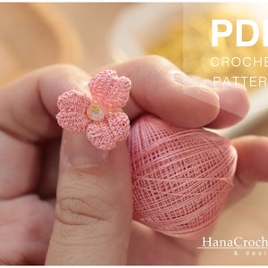 May include: A pink crochet flower with a white center, held in a hand with a ball of pink yarn. The image includes the text "PDF CROCHET PATTERN" and "HanaCrochet & design".