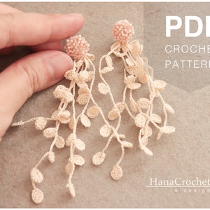 May include: A PDF crochet pattern for a pair of delicate, long, crocheted earrings with a pink beaded top. The earrings are made with white yarn and feature a cascading design of small, crocheted circles.