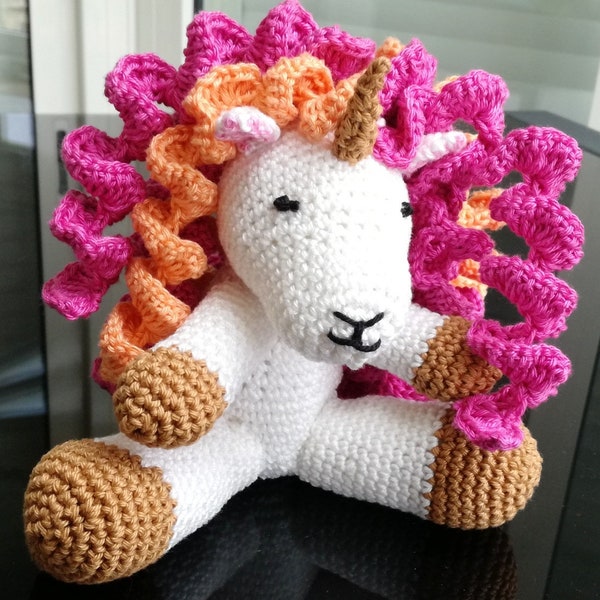 Licorne au crochet. Ce doudou a une abondante chevelure rose et orange pour amuser les petits doigts