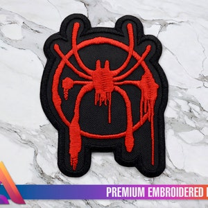 May include: A black and red embroidered patch featuring the Spider-Man: Into the Spider-Verse logo. The logo is a stylized spider with a red body and black legs, surrounded by a red circle.