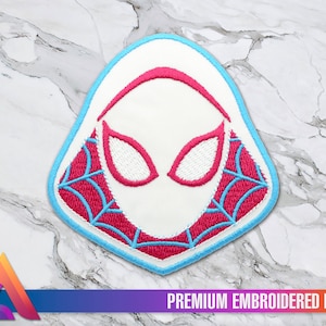 Op de afbeelding: Witte geborduurde patch met een roze en blauwe Spider-Man-maskerontwerp. De patch heeft een blauwe omtrek en een webpatroon.