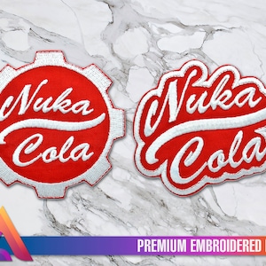 Op de afbeelding: Twee geborduurde patches met het Nuka Cola-logo. Eén patch is rood met witte letters en een wit tandwielontwerp. De andere patch is rood met witte letters en een gebogen ontwerp. Beide patches zeggen "Nuka Cola" in witte letters.