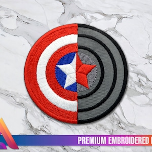 Puede incluir: Un parche redondo bordado con un dise&ntilde;o dividido. El lado izquierdo es un escudo de Capit&aacute;n Am&eacute;rica rojo, blanco y azul. El lado derecho es un escudo gris con c&iacute;rculos conc&eacute;ntricos.