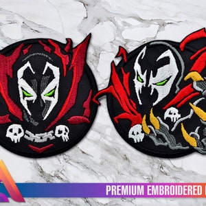 Könnte beinhalten: Zwei gestickte Patches mit dem Charakter Spawn. Der erste Patch ist eine Nahaufnahme von Spawns Gesicht mit roten und schwarzen Flammen. Der zweite Patch zeigt Spawn in Kampfpose mit roten und schwarzen Flammen und einer gelben Klaue.