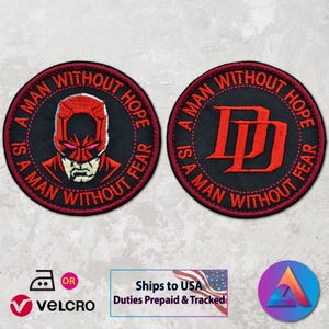 May include: Two round black patches with red embroidered text and designs. One patch features a red illustration of a character's face, the other displays the letters "DD". The text around the border reads "A MAN WITHOUT HOPE IS A MAN WITHOUT FEAR".