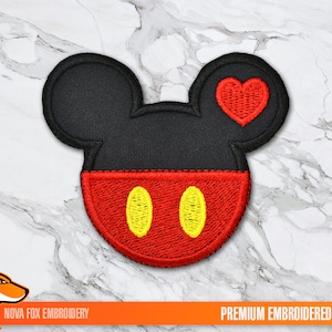 Peut inclure: Écusson brodé représentant la tête de Mickey Mouse avec un cœur rouge. L'écusson a une tête et des oreilles noires, un visage rouge avec deux formes ovales jaunes et un cœur rouge. Le texte "PREMIUM EMBROIDERED PATCH" est en bas.