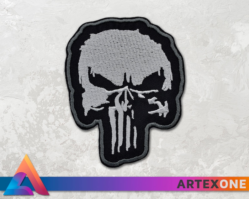 May include: A black and white embroidered patch of the Punisher skull. The skull is white with black outlines and details. The patch is made of fabric and has a stitched edge.