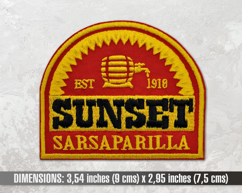 Op de afbeelding: Een geborduurde patch in rood, geel en zwart met de tekst "EST 1918 SUNSET SARSAPARILLA". De patch heeft een gestileerde afbeelding van een vat met een kraan. De patch is 9 cm bij 7,5 cm.