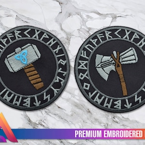 May include: Two embroidered patches, one with a silver hammer and the other with a silver axe. Both patches have a black background with a grey circle around the edges. The circle is inscribed with runes in grey.