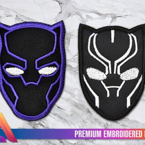 Può includere: Due toppe ricamate con la maschera di Black Panther. La toppa a sinistra ha un contorno viola e la toppa a destra ha un contorno bianco. Entrambe le toppe sono nere con occhi bianchi.
