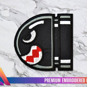 Könnte beinhalten: Schwarzer und weißer gestickter Aufnäher mit einem Videospielcharakter mit einem rot-weißen Mund. Der Aufnäher trägt unten den Schriftzug "PREMIUM EMBROIDERED PATCH".