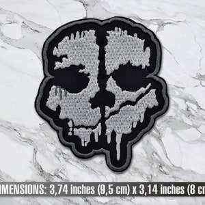 May include: A grey and black embroidered patch of a skull with dripping details. The patch measures 9.5 cm by 8 cm.