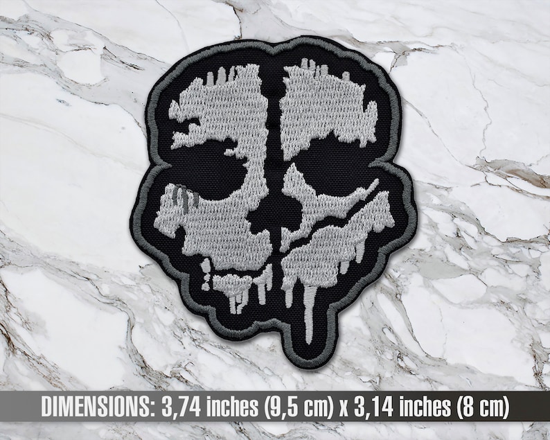 May include: A grey and black embroidered patch of a skull with dripping details. The patch measures 9.5 cm by 8 cm.