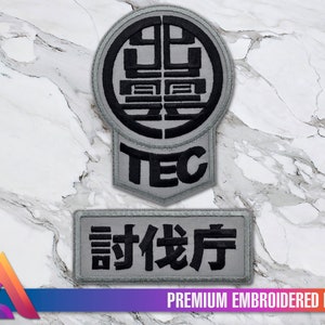 Pode incluir: Um remendo bordado cinza com um círculo preto contendo caracteres chineses e a palavra "TEC" abaixo. Um segundo remendo bordado cinza com os caracteres chineses "說俠房" está abaixo do primeiro remendo.