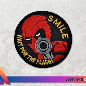 May include: A black and red embroidered patch with a character holding a gun. The text on the patch reads "SMILE WAIT FOR THE FLASH".
