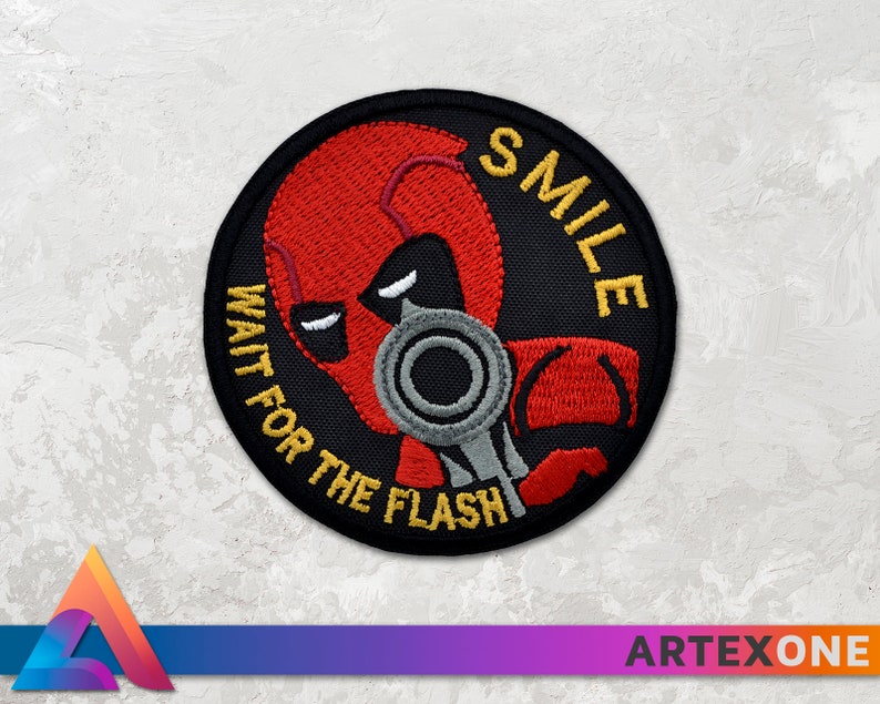 May include: A black and red embroidered patch with a character holding a gun. The text on the patch reads "SMILE WAIT FOR THE FLASH".
