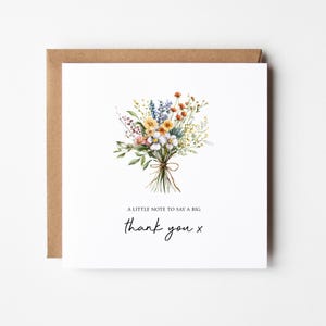 May include: A square white greeting card featuring a watercolor illustration of a wildflower bouquet tied with a brown string. Below the flowers, the text reads A LITTLE NOTE TO SAY A BIG thank you x. The card is paired with a brown kraft envelope.