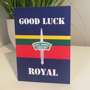 May include: A blue card with the text "GOOD LUCK" in white letters. A white dagger with a green, yellow, and red stripe pattern behind it. The dagger has a white patch with the text "ROYAL MARINES COMMANDO" in black letters. The text "ROYAL" is in white letters at the bottom of the card.