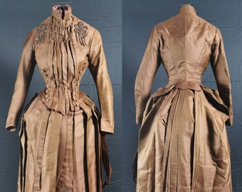 May include: A brown silk dress with a fitted bodice and a full skirt. The dress features intricate beaded embellishments on the bodice and skirt.
