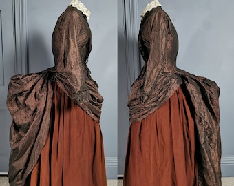 May include: A brown and black brocade dress with a fitted bodice and a full skirt. The skirt is gathered at the waist and has a train. The dress is accented with a lace collar.