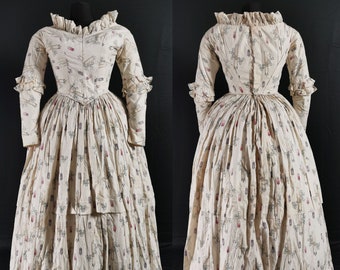 May include: A white dress with a floral pattern and a ruffled neckline. The dress has a fitted bodice and a full skirt.
