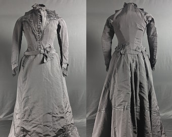 May include: A black long-sleeved dress with a fitted bodice and a full skirt. The dress has a lace trim around the neckline and cuffs. The skirt has a tiered design with lace trim at the hem.