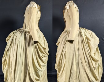 May include: A vintage-style dress with a gathered skirt and long sleeves. The dress is made of a light-colored fabric and has a simple, elegant design.