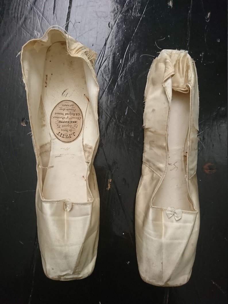 May include: A pair of white satin ballet slippers with a label inside one slipper that reads "S. de Paris, Be-Agent Se, MRENOTTE, 124. Regent Street, Private door, LONDON".