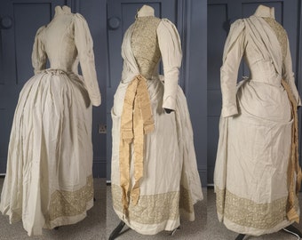 May include: A white dress with a long skirt and long sleeves. The dress has a fitted bodice and a gathered skirt. The dress is trimmed with a gold-colored lace.