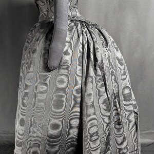 May include: A vintage gray dress with a unique pattern, featuring a fitted bodice and a full skirt. The dress has a high neckline and short sleeves. The fabric has a textured, swirling design. The dress is displayed on a mannequin.