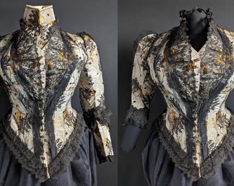 Puede incluir: Una blusa vintage de color blanco y dorado con ribetes de encaje negro. La blusa tiene un cuello alto y mangas largas. El encaje está en el cuello, las mangas y el dobladillo de la blusa.