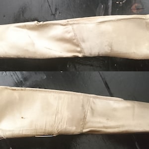 May include: A pair of off-white satin slippers with frayed edges. The slippers are worn and have a pointed toe.