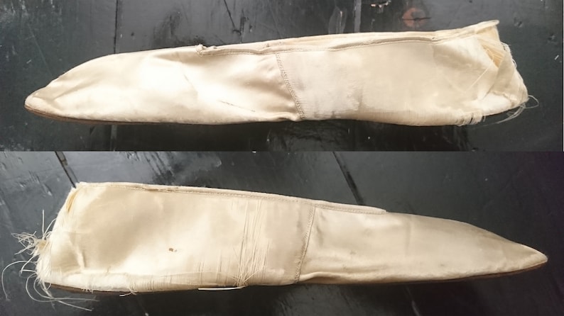 May include: A pair of off-white satin slippers with frayed edges. The slippers are worn and have a pointed toe.