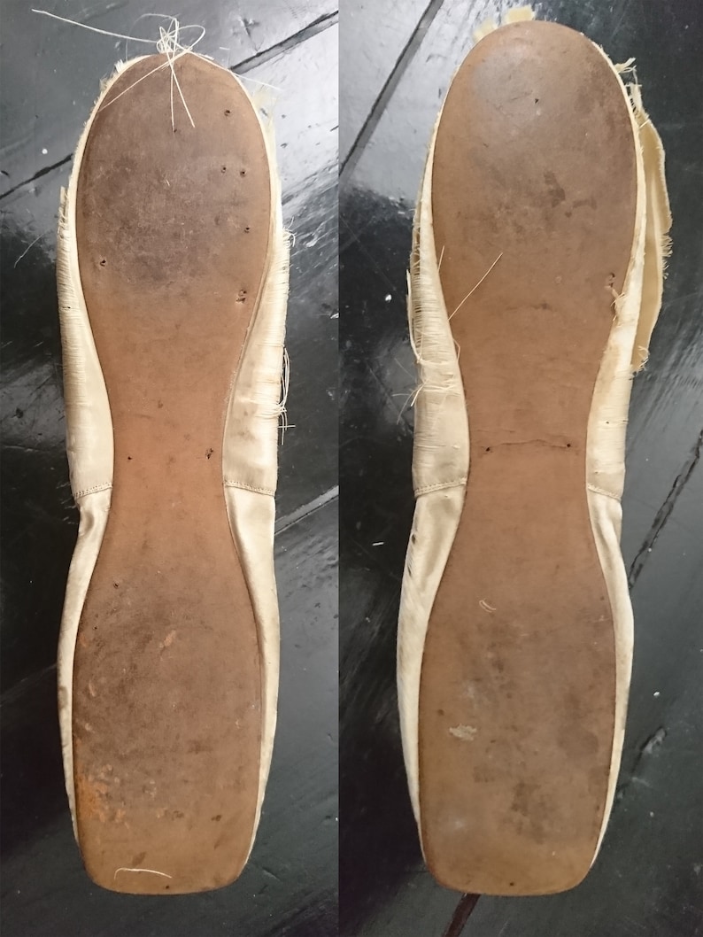 May include: A pair of white satin ballet shoes with worn leather soles. The shoes are slightly frayed around the edges.