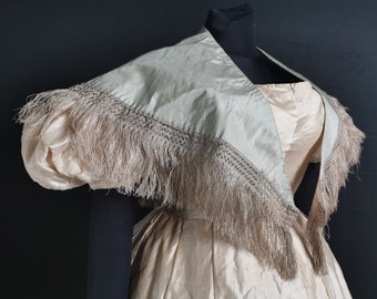 May include: A pale pink satin dress with a light green silk shawl. The shawl has a crocheted trim and a fringe of brown feathers.
