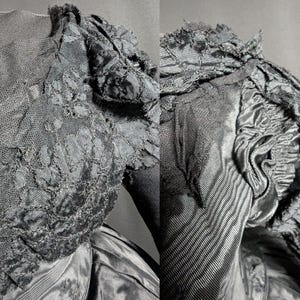 May include: Close-up of a black vintage dress bodice. The dress features intricate lace detailing on the sleeves and bodice, with a textured, layered design. The fabric appears to be a combination of satin and lace, creating a rich, dark aesthetic.