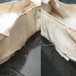 May include: A pair of beige fabric ballet slippers with frayed edges. The slippers are unlined and have a white cotton filling.