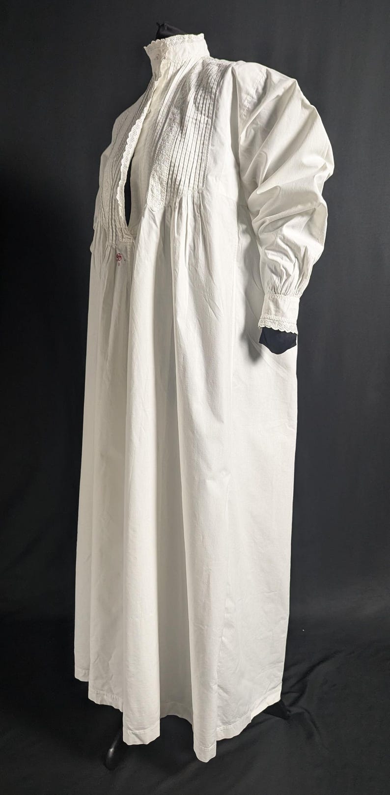 May include: A long, white nightgown with a high collar and long sleeves. The nightgown features decorative pleats and lace detailing on the bodice and cuffs. The garment is made of a lightweight fabric.