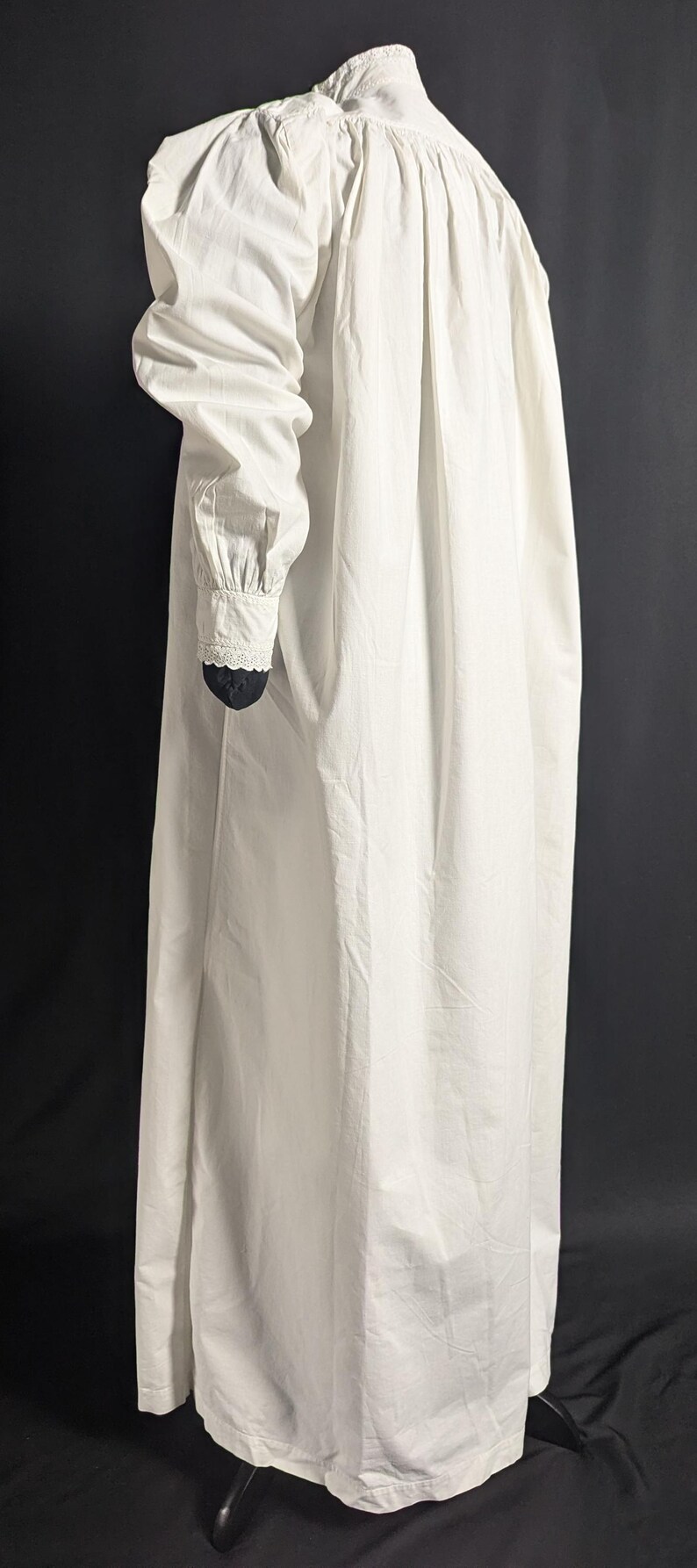 May include: A long, white nightgown with a high collar and long sleeves. The sleeves have a gathered design at the shoulder and a lace trim at the wrist. The nightgown is made of a lightweight fabric.