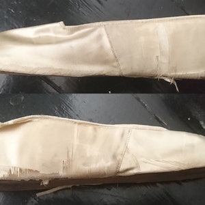 May include: A pair of off-white satin ballet slippers with frayed edges and a pointed toe.