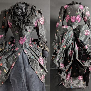Puede incluir: Un vestido de seda negro con estampado floral en tonos rosa, morado y verde. El vestido tiene un corpiño ajustado y una falda completa con un vuelo.