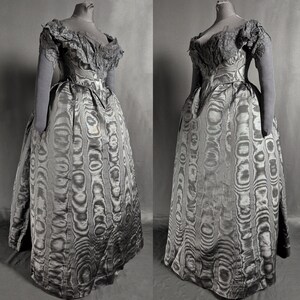 May include: A vintage gray dress with a unique pattern, displayed on a mannequin. The dress features a fitted bodice, a full skirt, and delicate lace detailing on the shoulders and sleeves. The fabric has a swirling, wood-grain-like design.