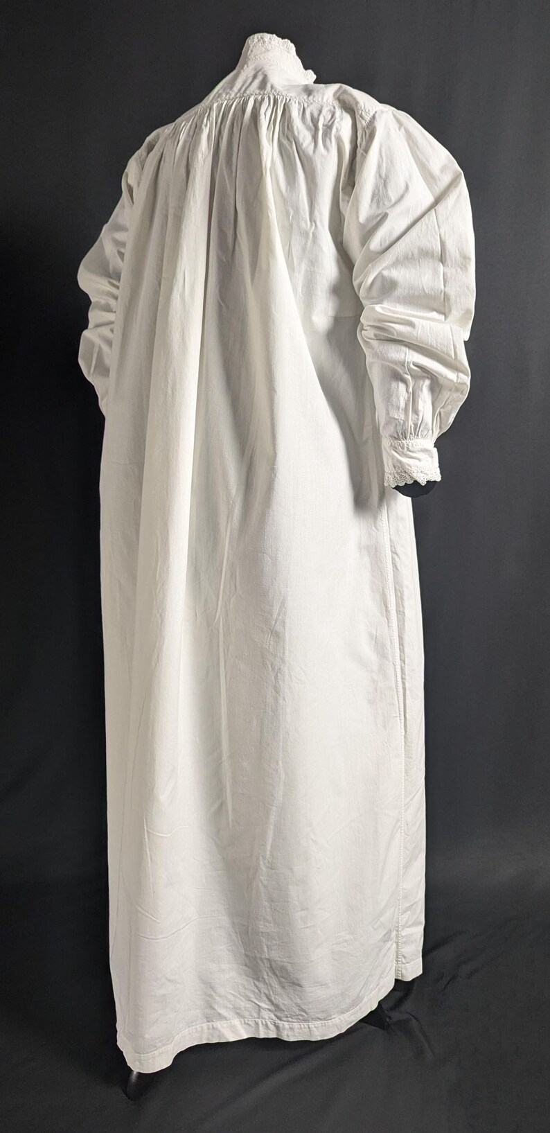 May include: A long, white cotton nightgown with long sleeves and a high, ruffled collar. The sleeves have buttoned cuffs with lace trim. The gown is gathered at the shoulders and falls to the floor.