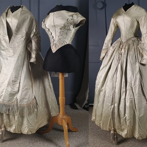 May include: A vintage ivory silk wedding dress with a long train and a fitted bodice. The dress has a lace trim and a tassel at the bottom.