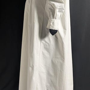 May include: A long, white nightgown with long sleeves and a high collar. The nightgown features delicate lace detailing on the collar and cuffs. The fabric appears to be a lightweight cotton or linen, suitable for sleepwear. The garment is displayed against a dark background.