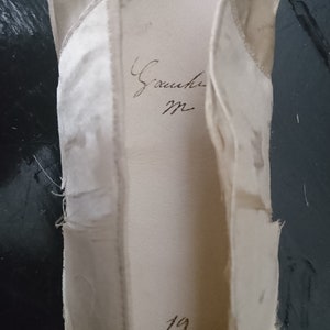 May include: A white satin ballet shoe with the inscription "Gauche" and the number "19" written inside.